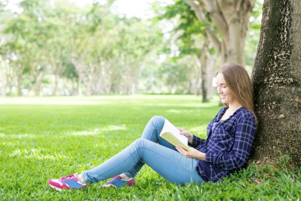 Mujer sentada en el pasto leyendo un libro en un espacio verde y salud mental