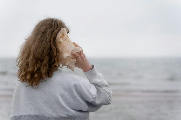 Mujer en el mar escuchando una concha marina